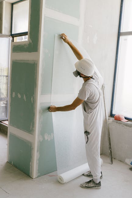 Construction worker in hard hat applying wallpaper inside a building under renovation.